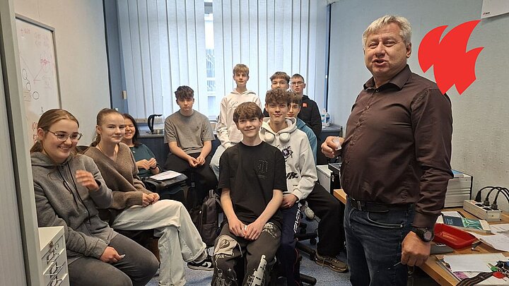 Grupa młodzich ludzi w laboratorium z prowadzącym, patrząw obiektyw. 